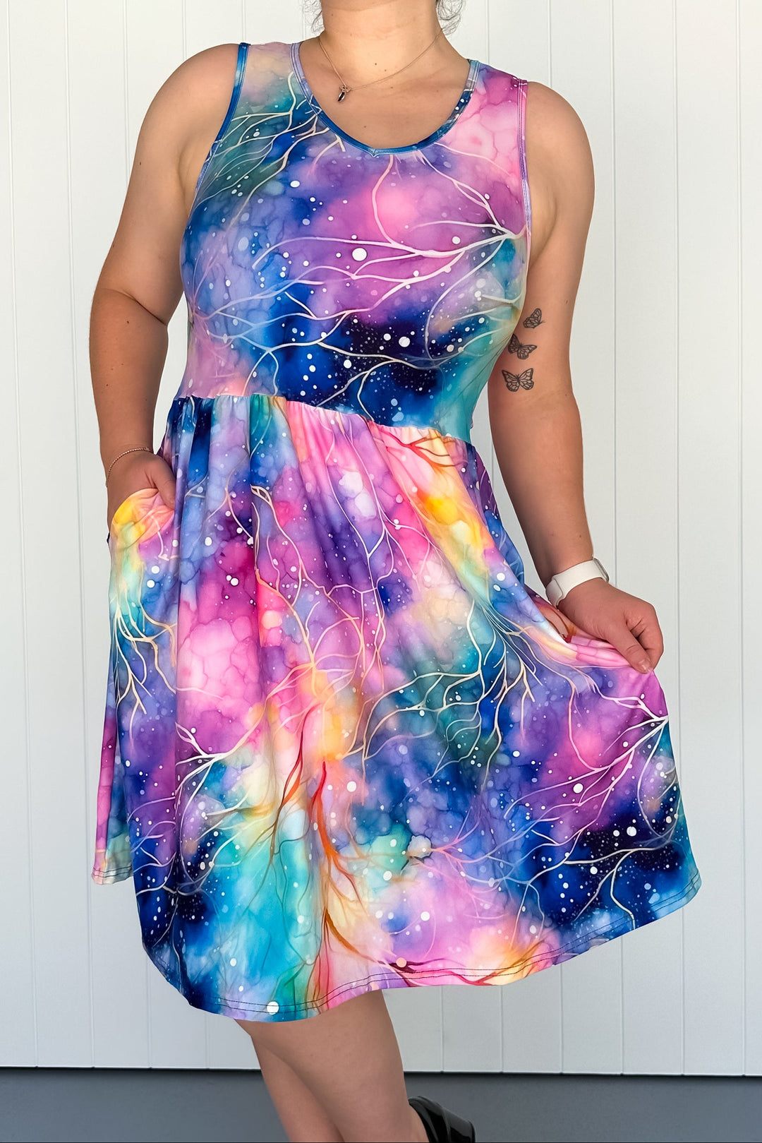 A sleeveless knee-length dress with side pockets featuring a vibrant multicolored tie-dye-like pattern.