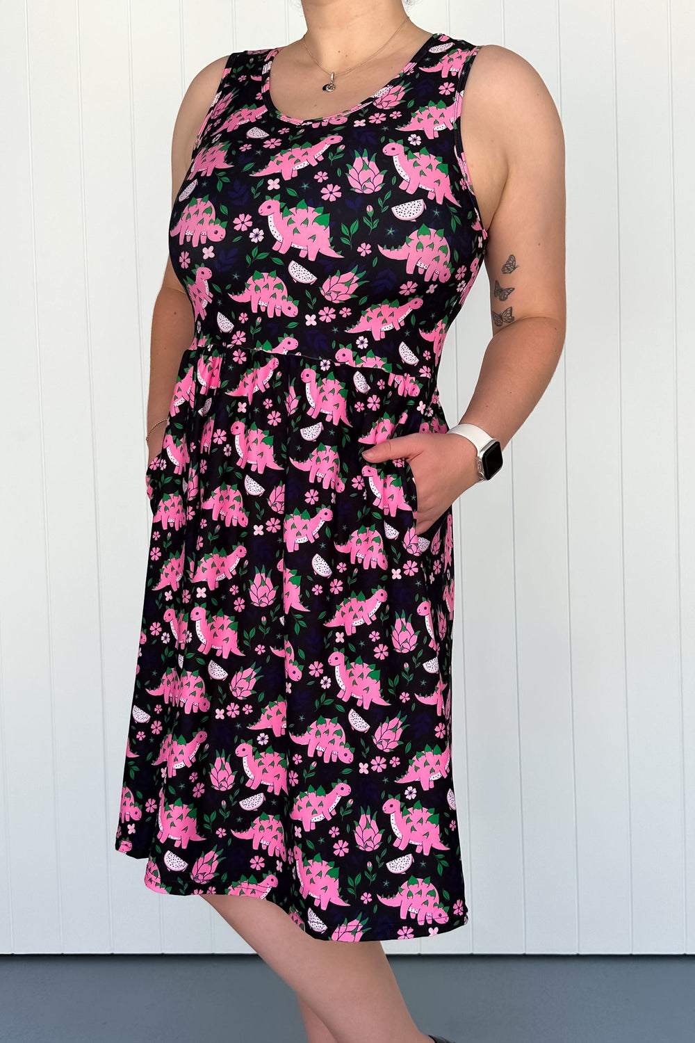 Person wearing a sleeveless dress with pink dinosaur pattern against a white background