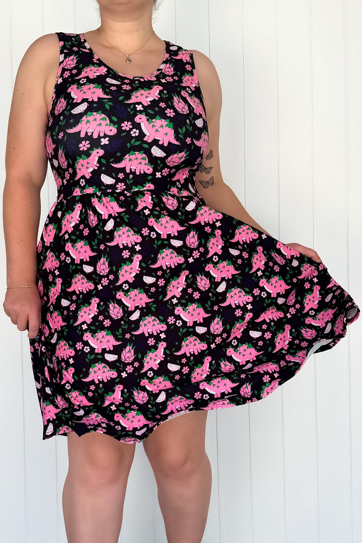 A sleeveless knee-length black dress with a pink dinosaur and dragon fruit print, featuring side pockets.