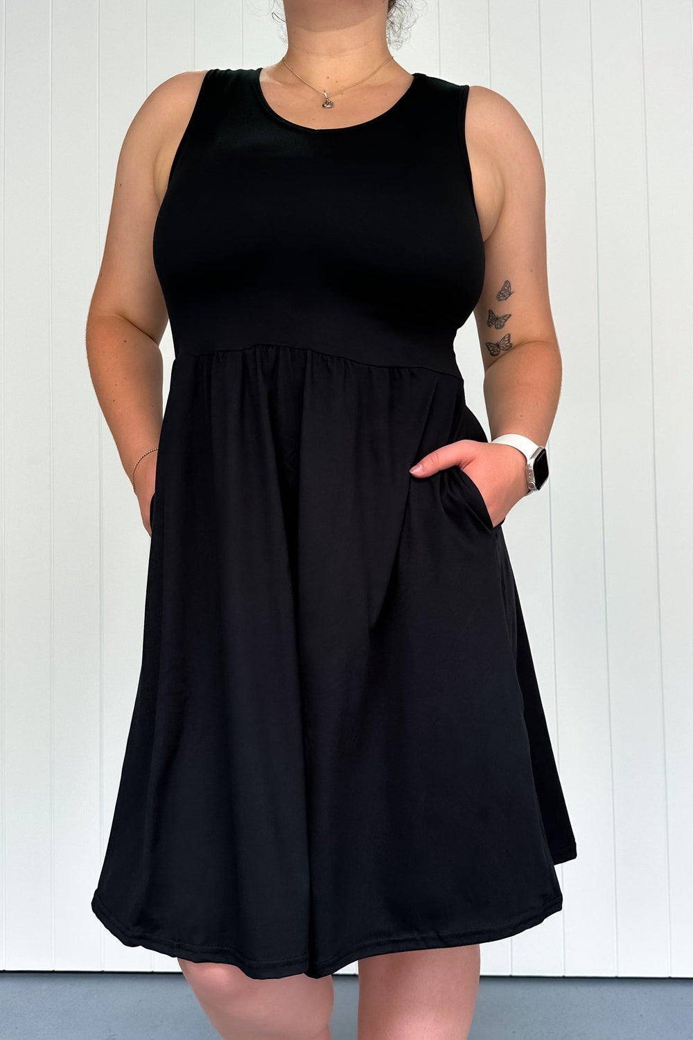 A model wearing a black sleeveless knee-length dress with a V-neck and side pockets.