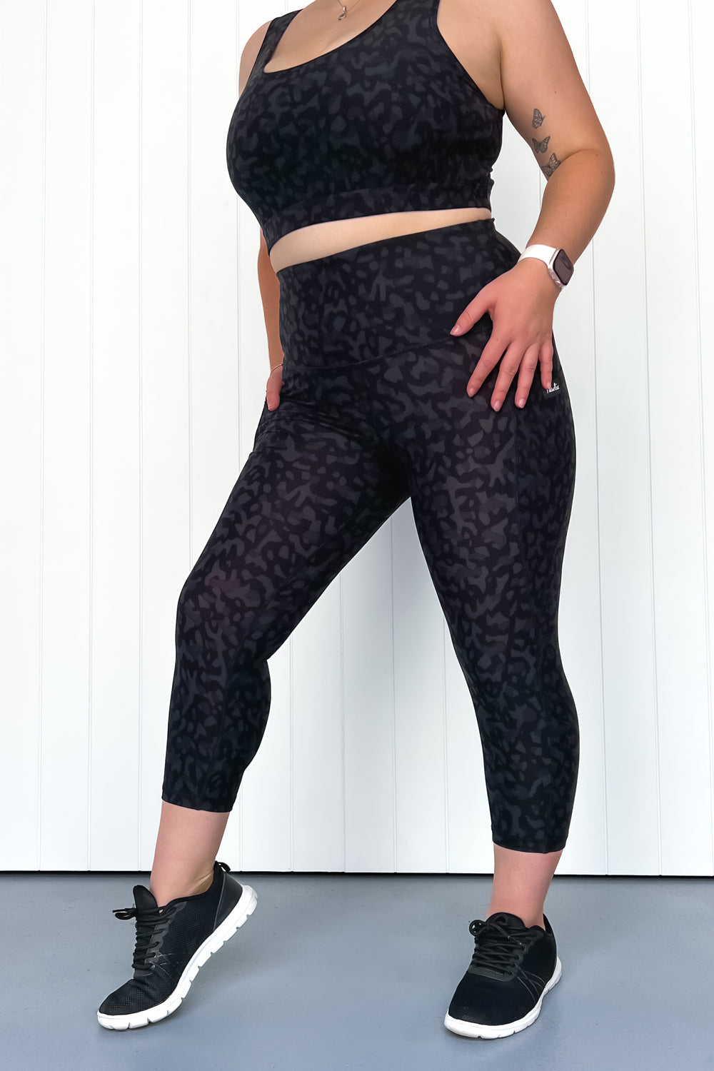 Person wearing black leopard print leggings and sports bra against a white background
