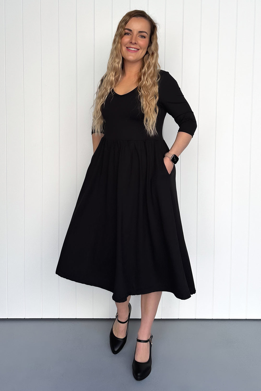 Woman wearing a black dress standing against a white wall.
