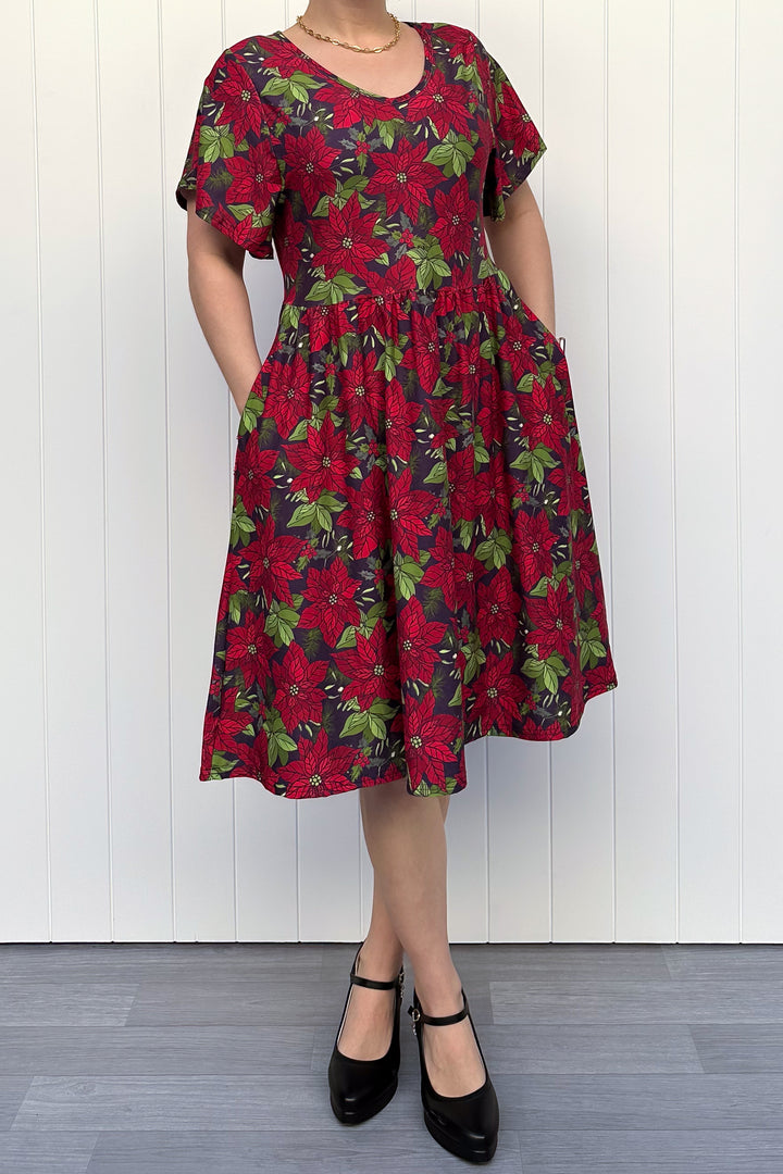 Person wearing red floral Christmas dress, standing against a white wall.