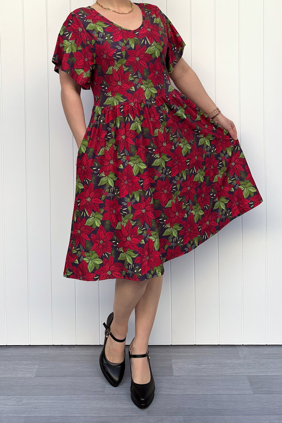 Person wearing red floral Christmas dress, standing against a white wall.