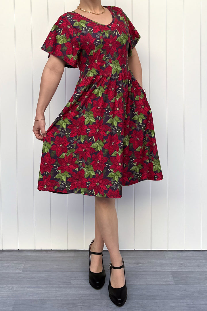 Person wearing red floral Christmas dress, standing against a white wall.