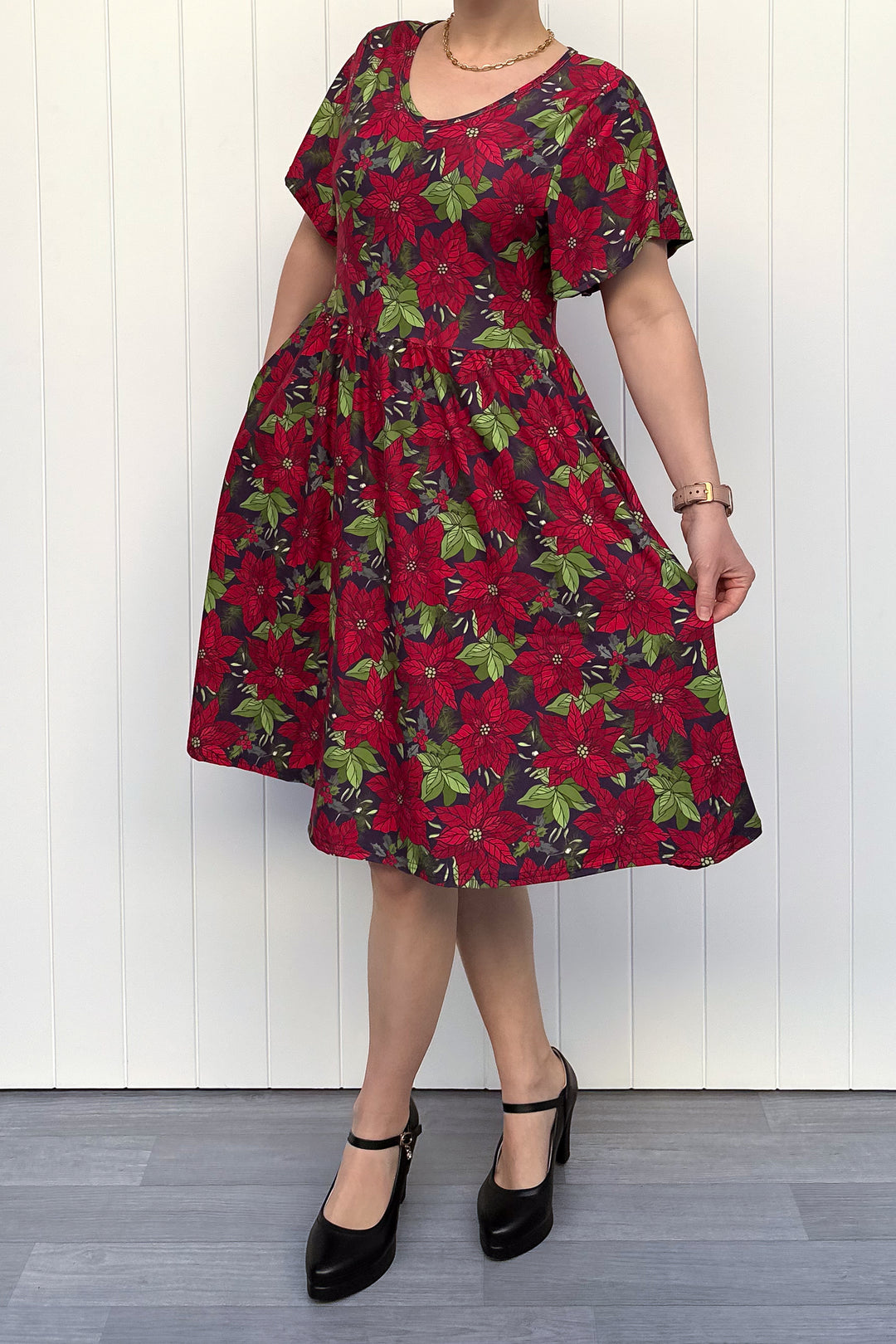 Person wearing red floral Christmas dress, standing against a white wall.
