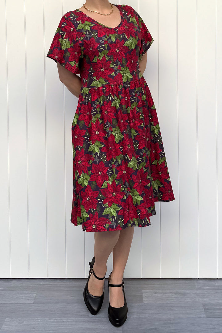 Person wearing red floral Christmas dress, standing against a white wall.