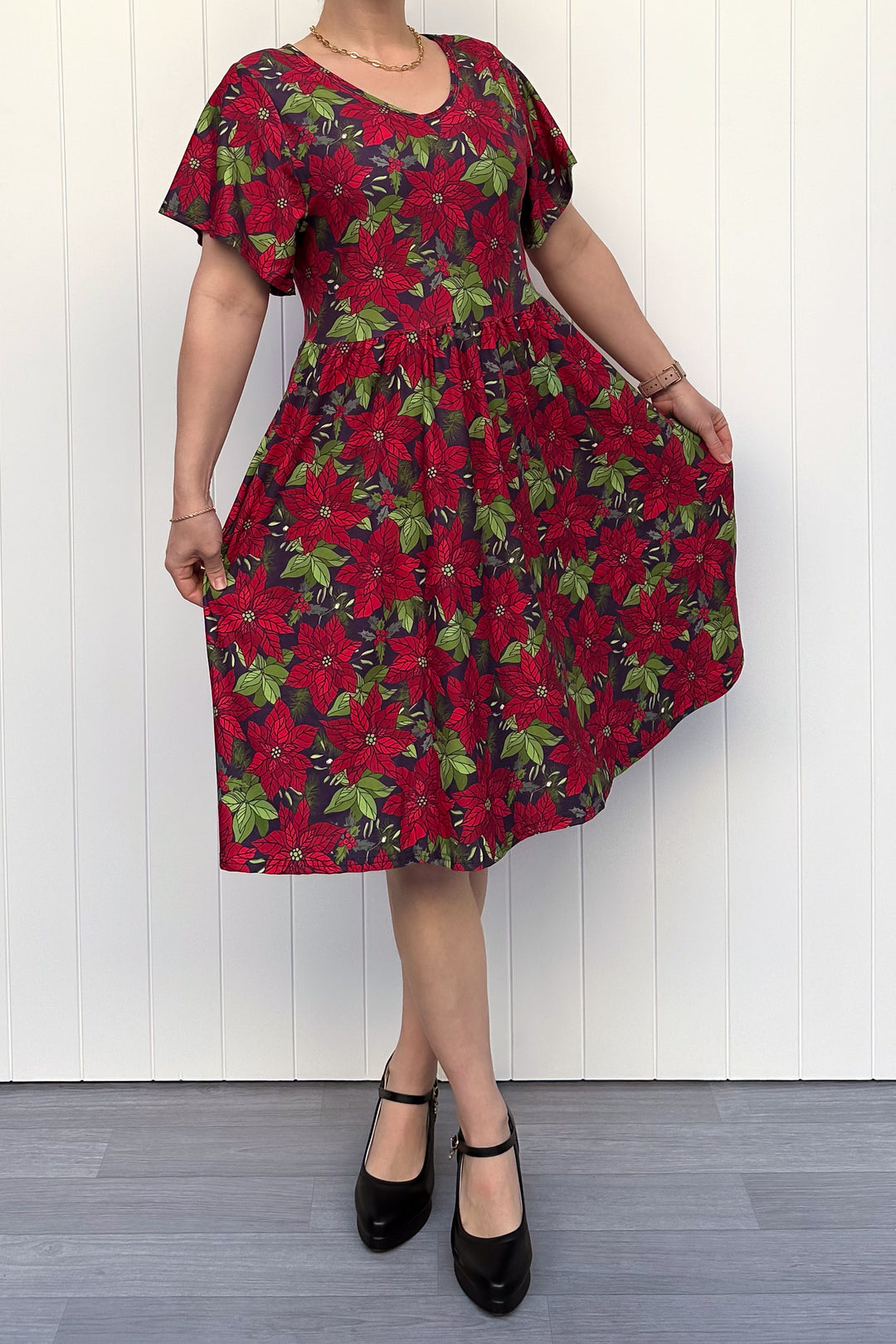Person wearing red floral Christmas dress, standing against a white wall.