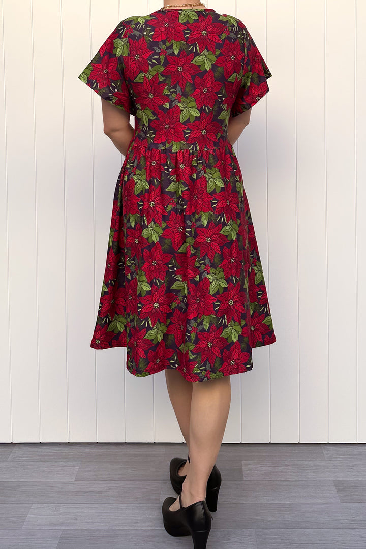 Person wearing red floral Christmas dress, standing against a white wall.