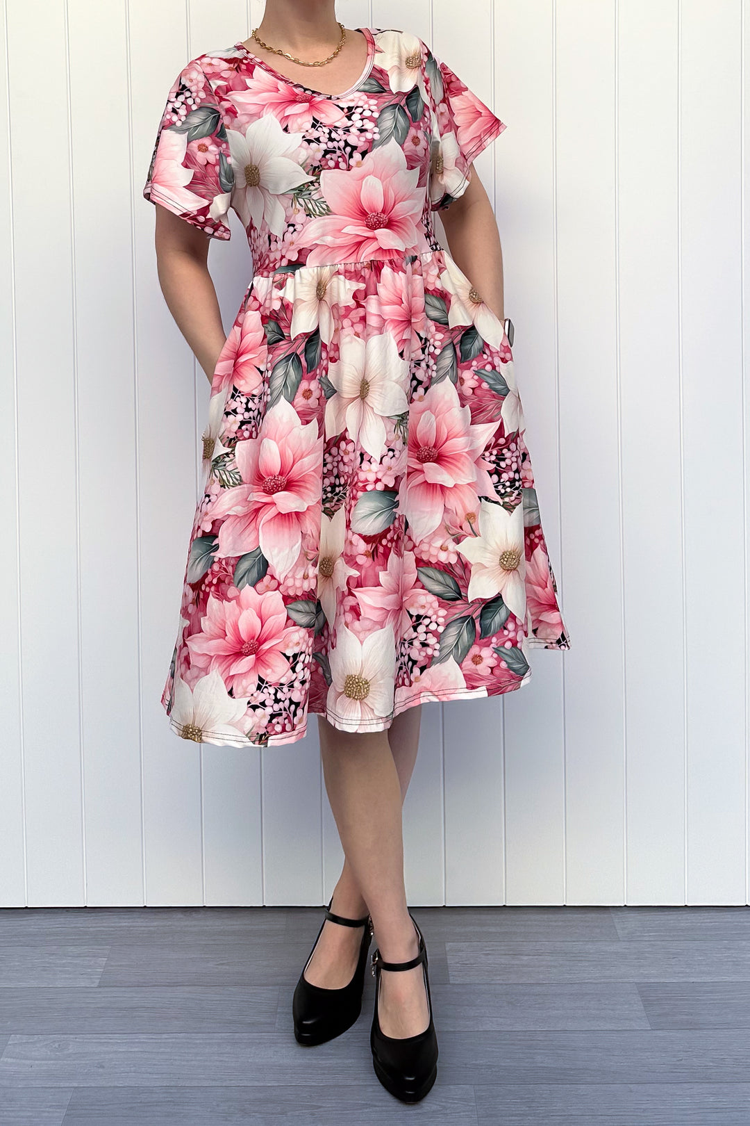 Person wearing a pink and cream floral dress standing in front of white background


