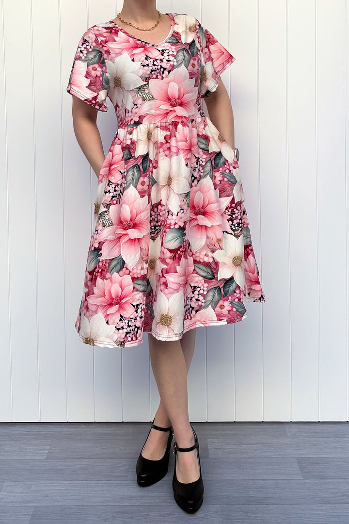 Person wearing a pink and cream floral dress standing in front of white background

