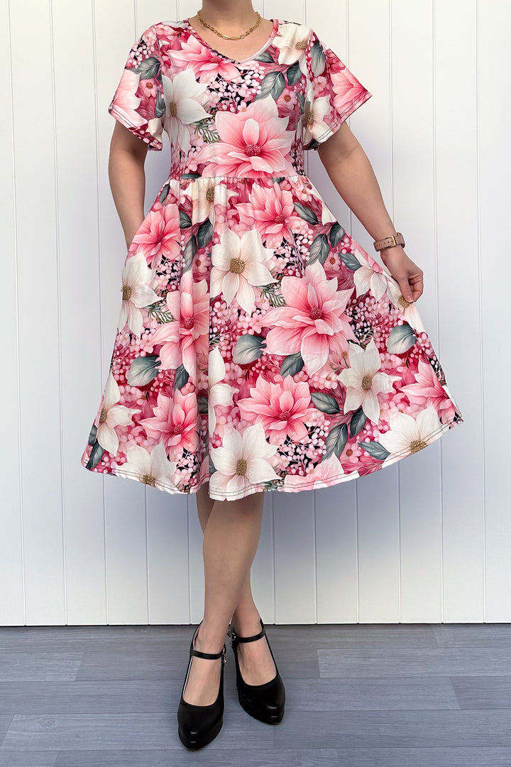 Person wearing a pink and cream floral dress standing in front of white background