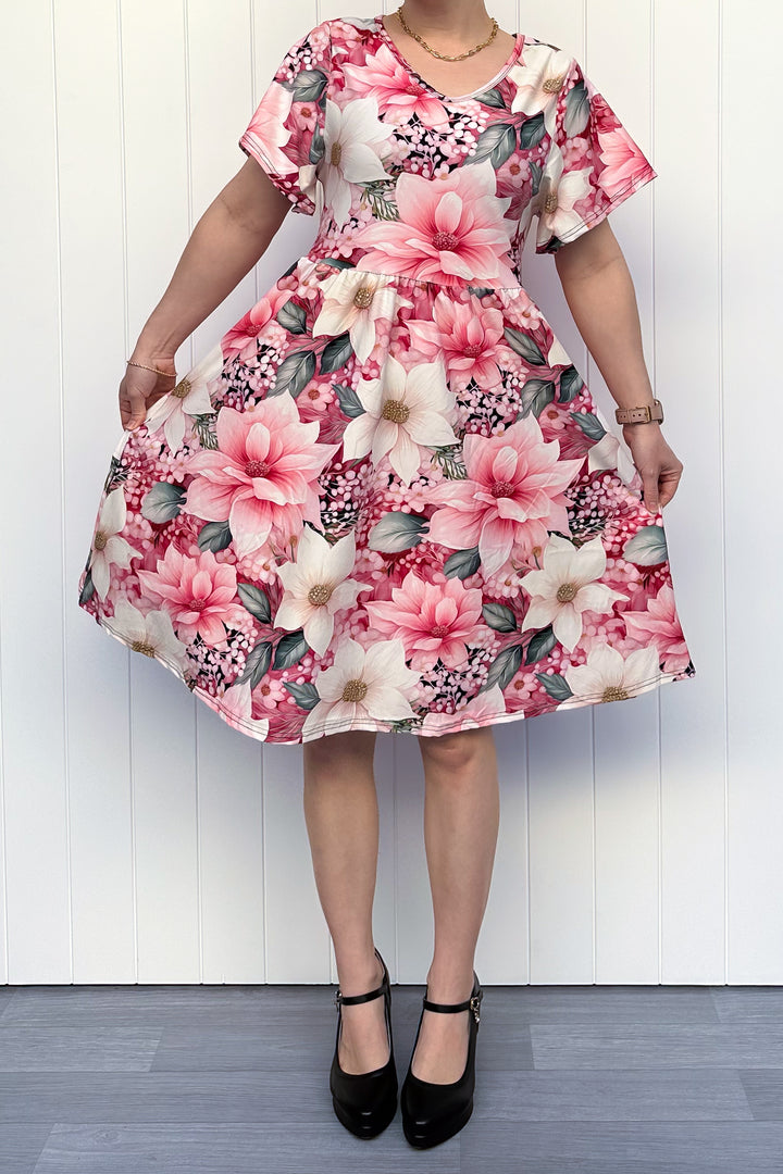 Person wearing a pink and cream floral dress standing in front of white background