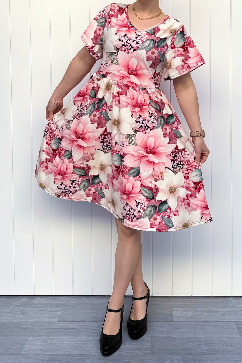 Person wearing a pink and cream floral dress standing in front of white background