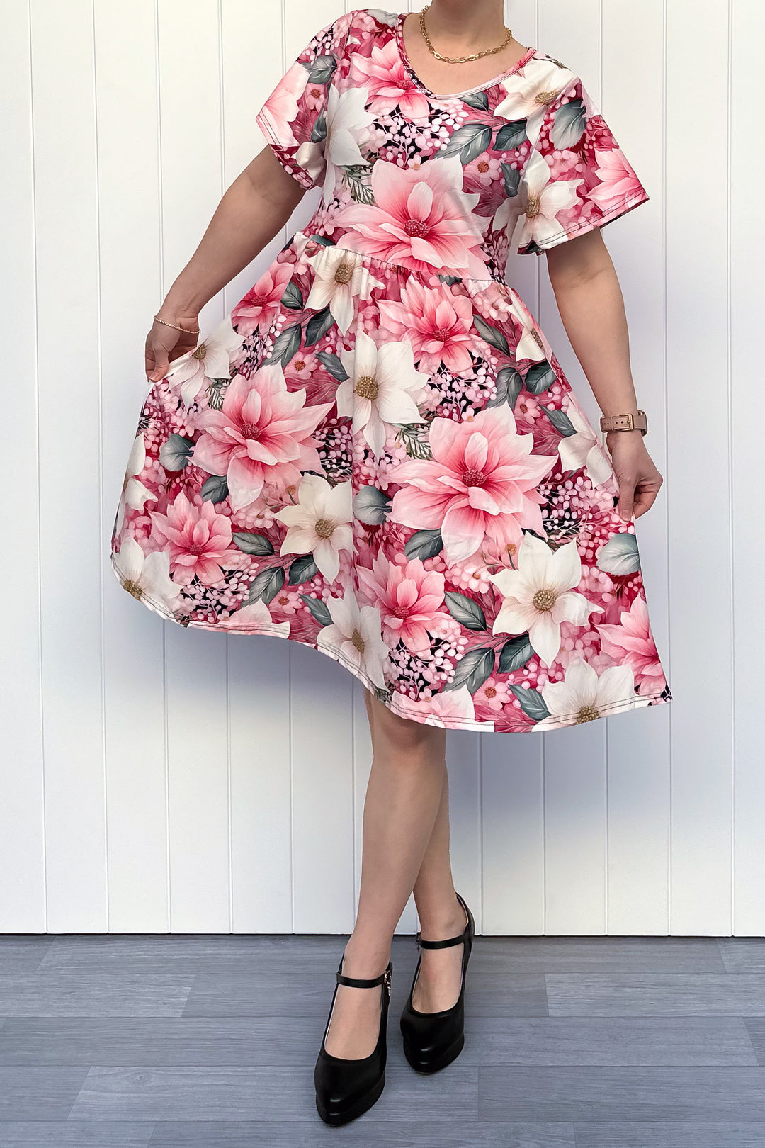 Person wearing a pink and cream floral dress standing in front of white background