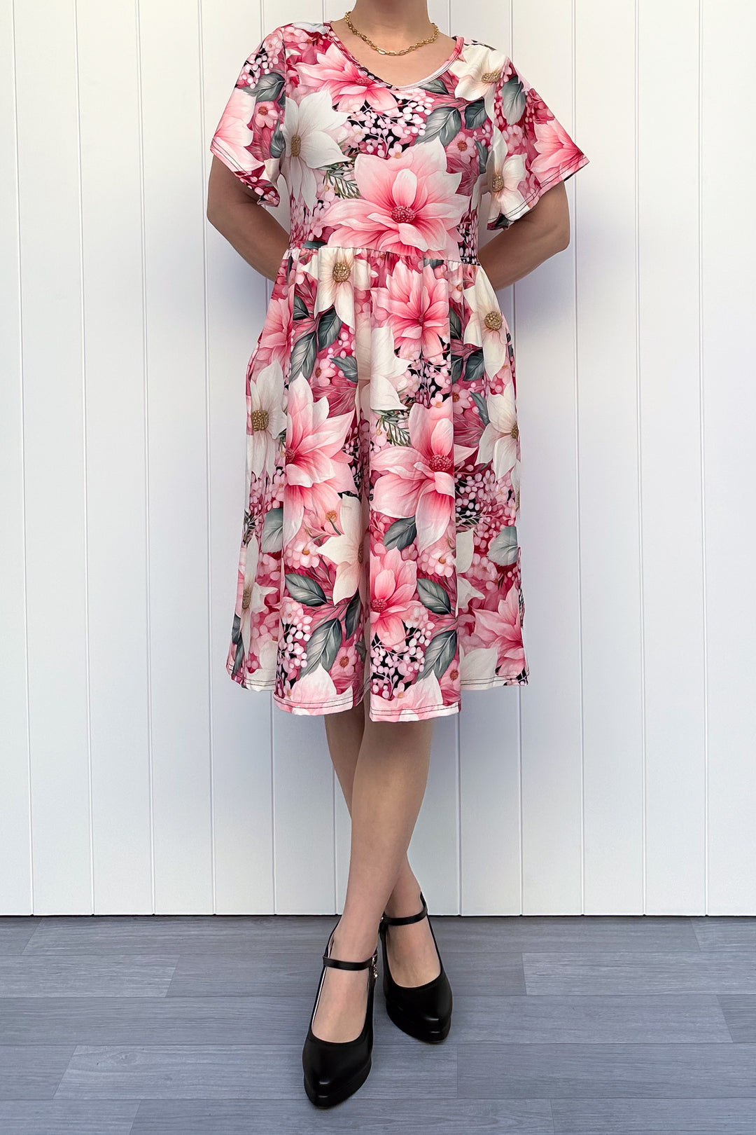 Person wearing a pink and cream floral dress standing in front of white background