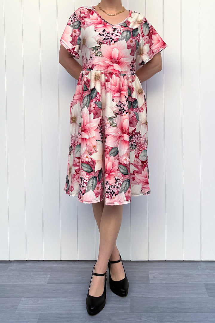 Person wearing a pink and cream floral dress standing in front of white background