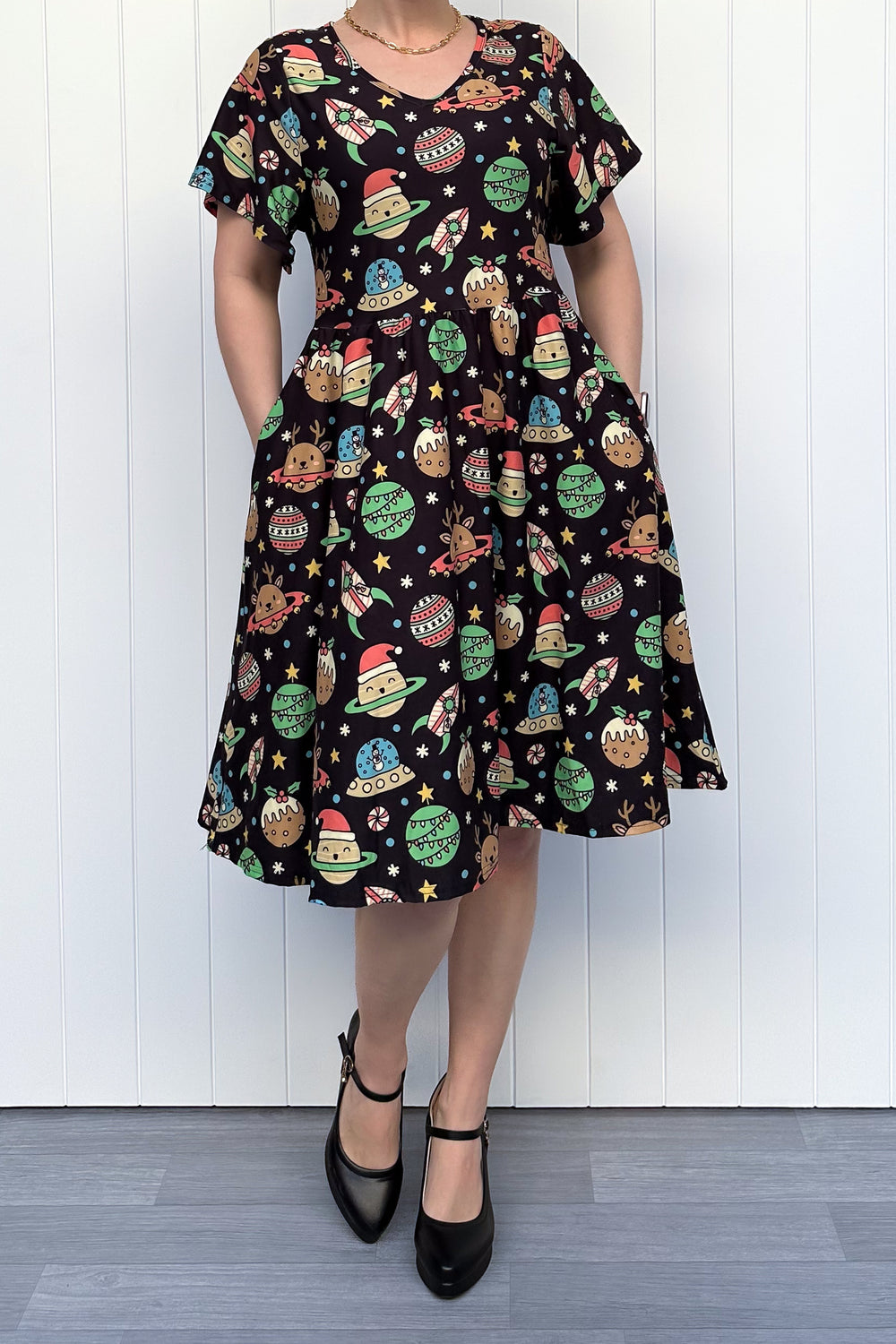 Person wearing a black dress with colorful space-themed Christmas pattern standing against a white wall.