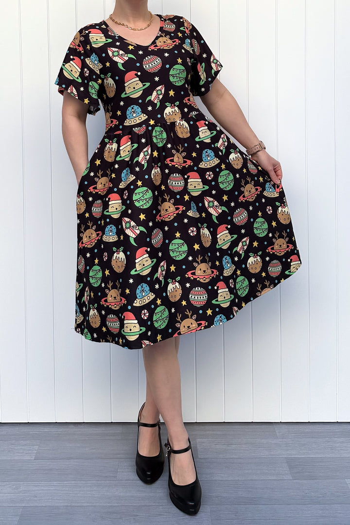 Person wearing a black dress with colorful space-themed Christmas pattern standing against a white wall.