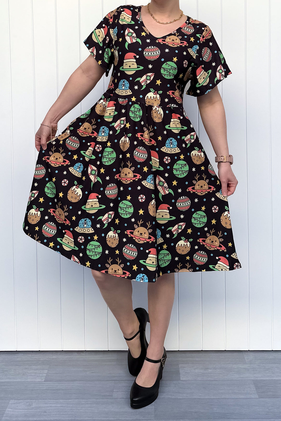 Person wearing a black dress with colorful space-themed Christmas pattern standing against a white wall.