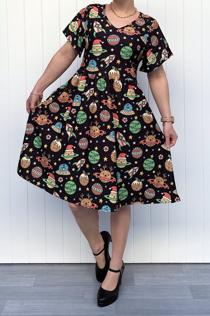 Person wearing a black dress with colorful space-themed Christmas pattern standing against a white wall.