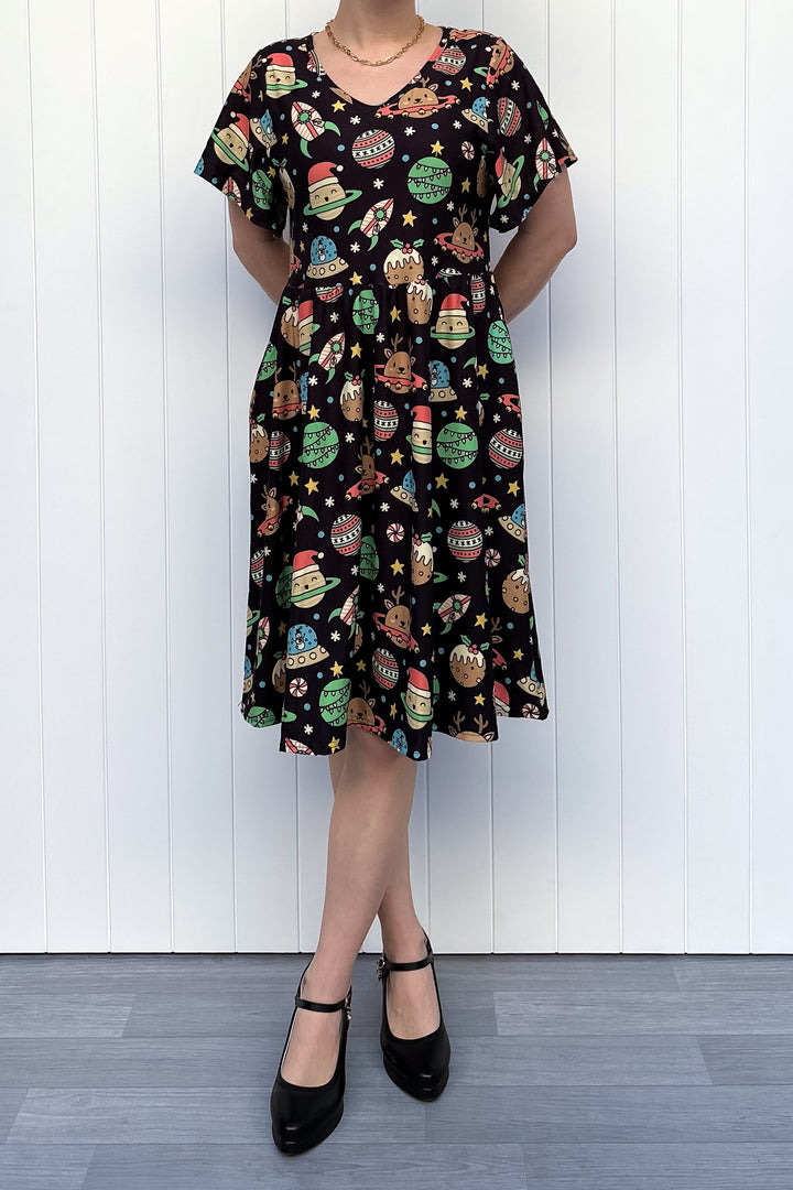 Person wearing a black dress with colorful space-themed Christmas pattern standing against a white wall.