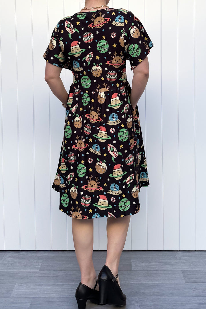 Person wearing a black dress with colorful space-themed Christmas pattern standing against a white wall.