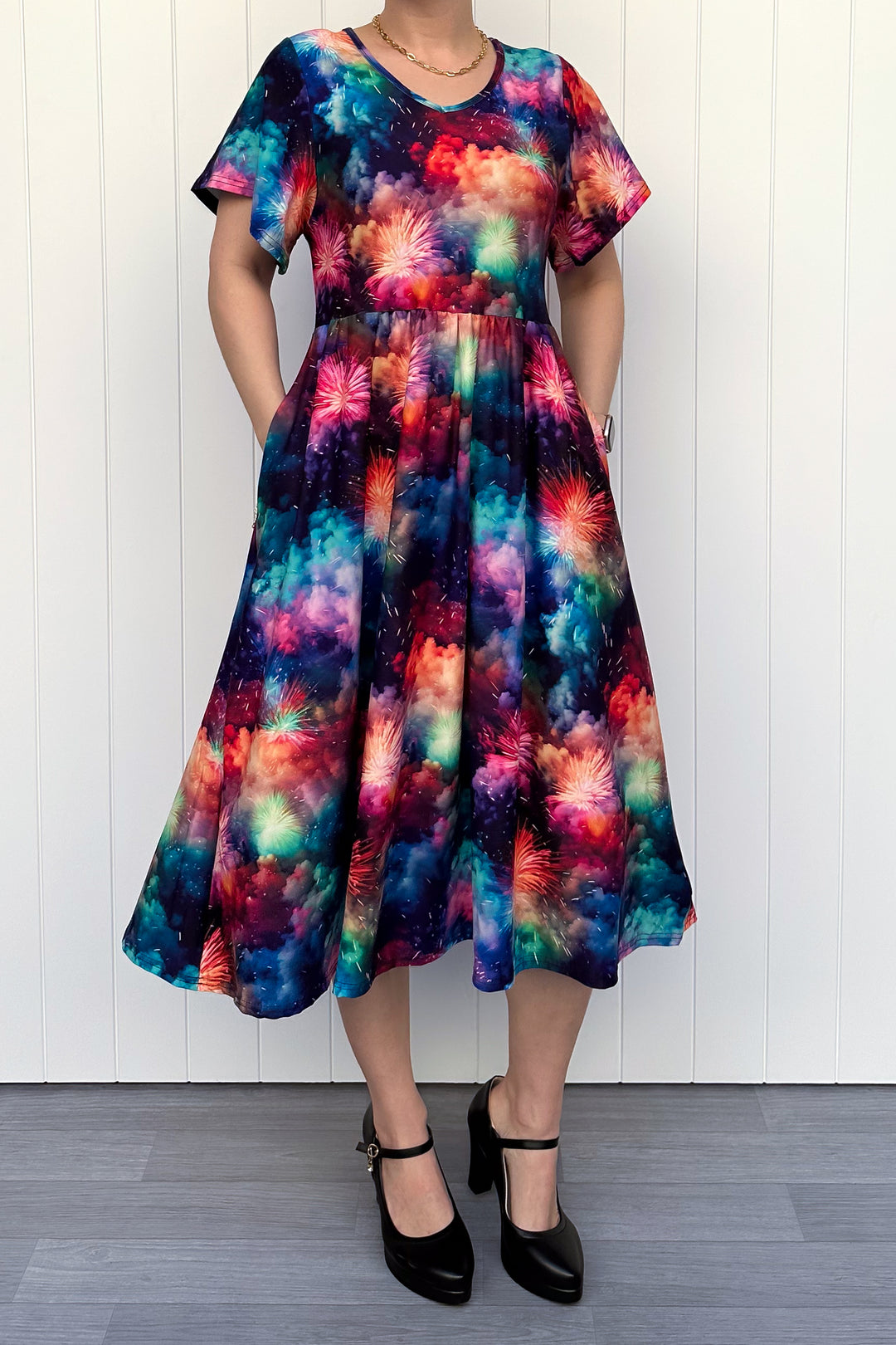 Person wearing a colorful firework patterened dress, standing against a white wall.