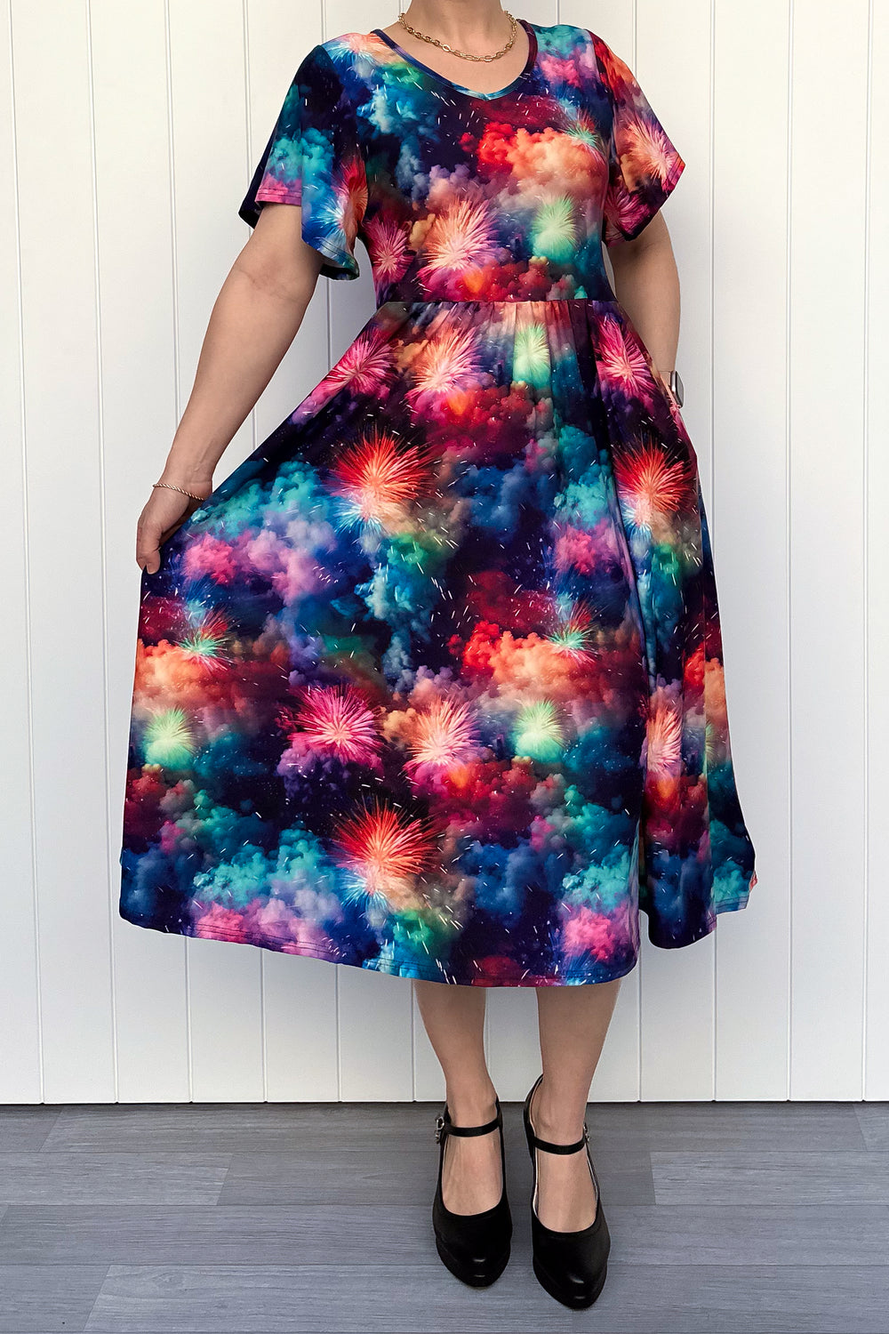 Person wearing a colorful firework patterened dress, standing against a white wall.
