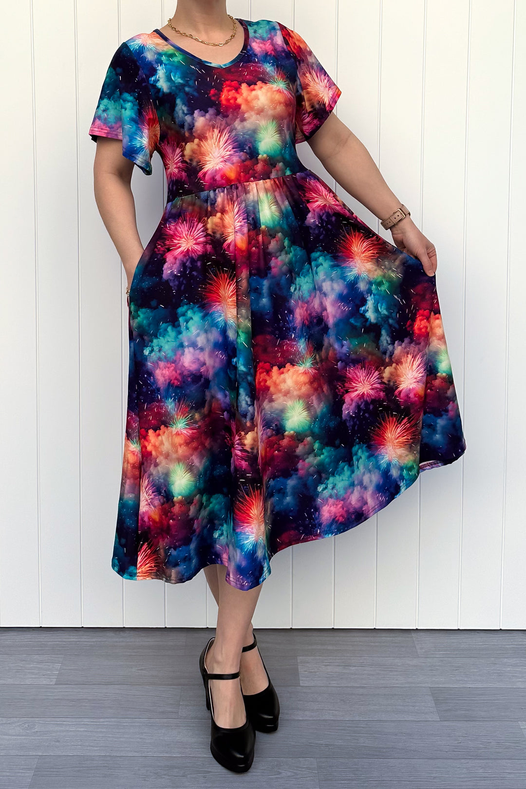 Person wearing a colorful firework patterened dress, standing against a white wall.