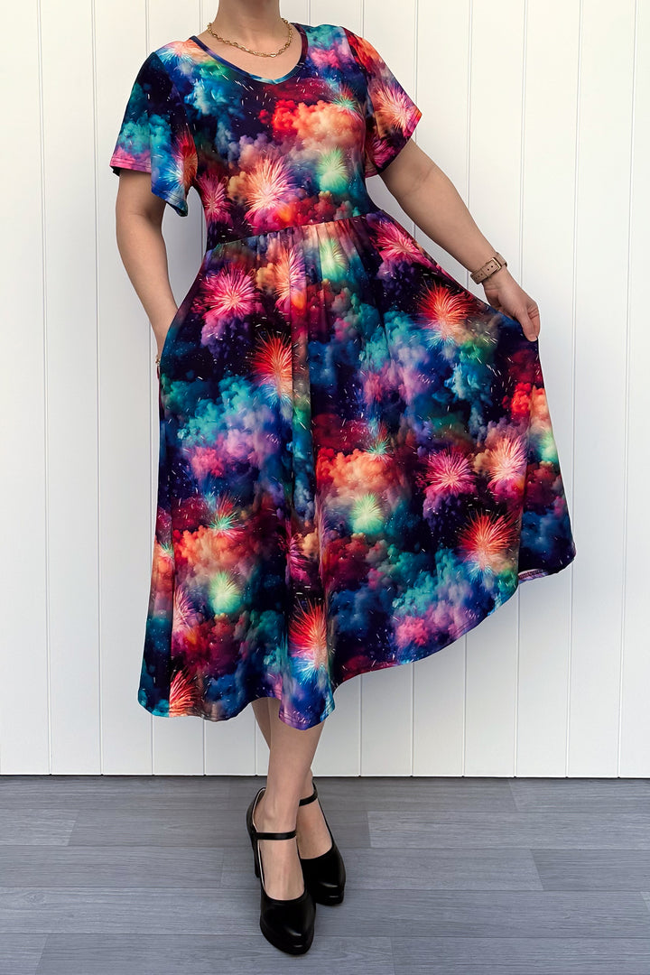 Person wearing a colorful firework patterened dress, standing against a white wall.