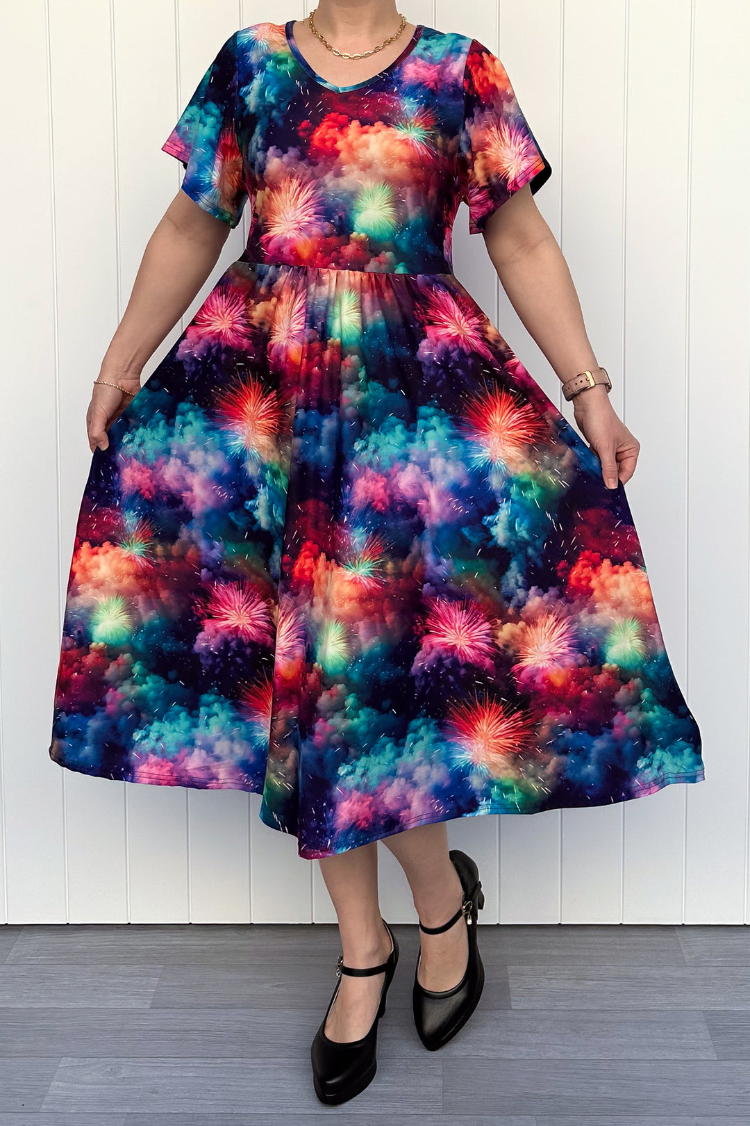 Person wearing a colorful firework patterened dress, standing against a white wall.
