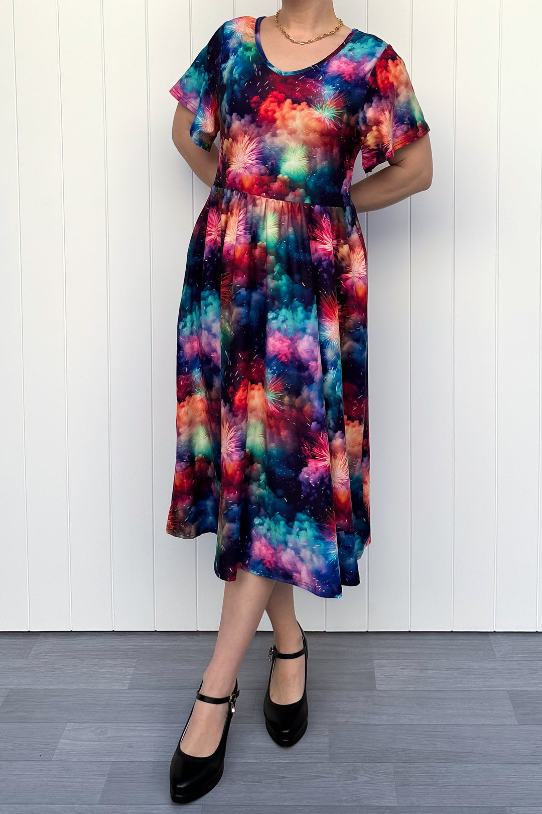 Person wearing a colorful firework patterened dress, standing against a white wall.