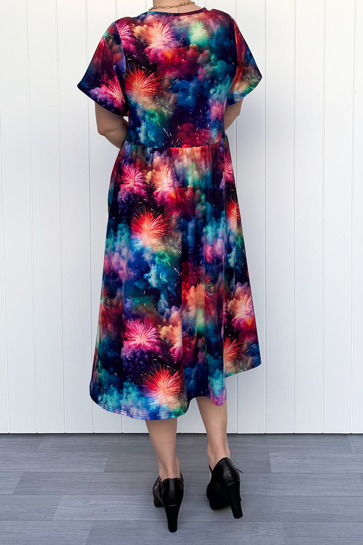 Person wearing a colorful firework patterened dress, standing against a white wall.