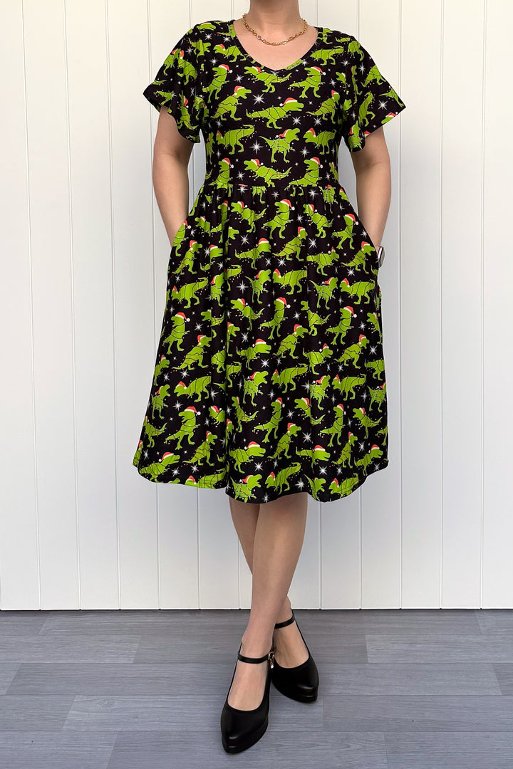 Person wearing a dress with green dinosaurs wearing santa hats on a black background.