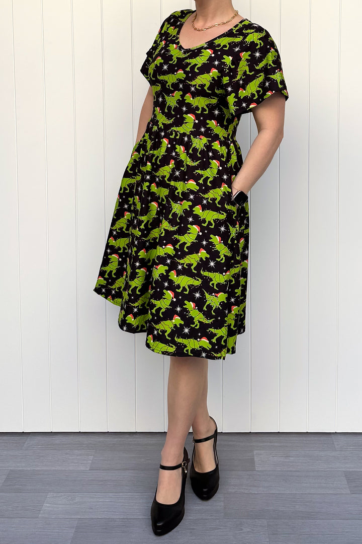 Person wearing a dress with green dinosaurs wearing santa hats on a black background.