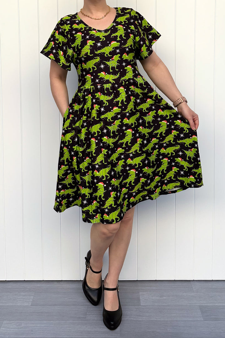 Person wearing a dress with green dinosaurs wearing santa hats on a black background.