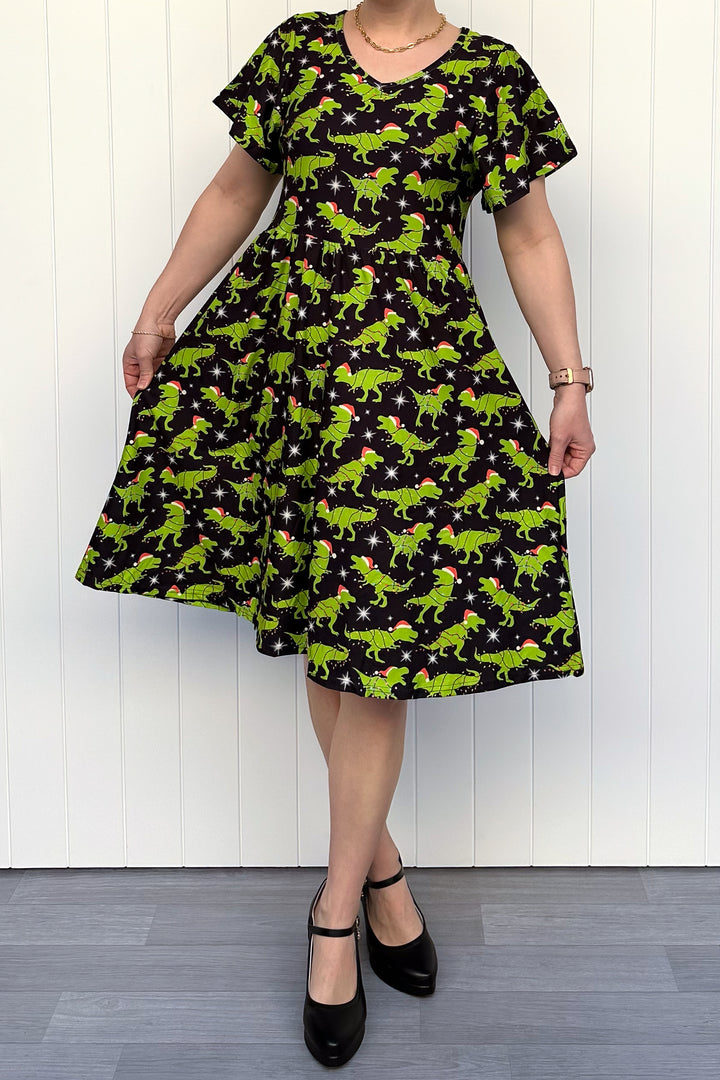 Person wearing a dress with green dinosaurs wearing santa hats on a black background.