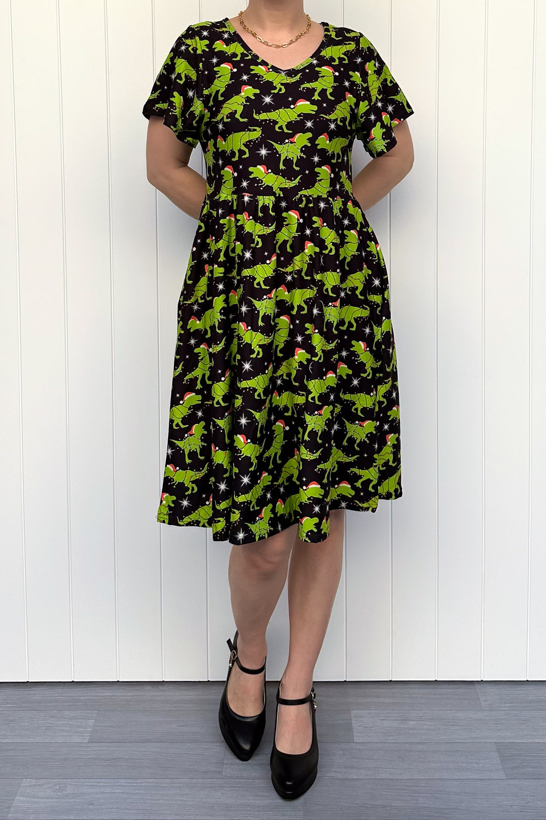 Person wearing a dress with green dinosaurs wearing santa hats on a black background.