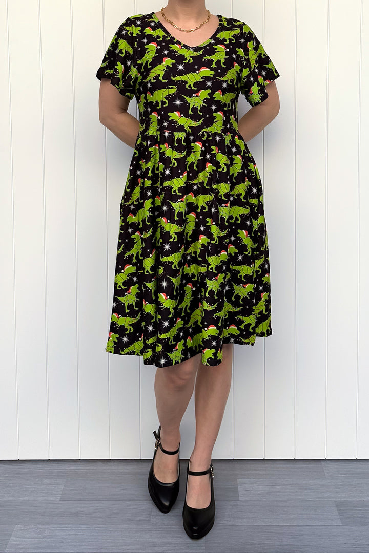Person wearing a dress with green dinosaurs wearing santa hats on a black background.