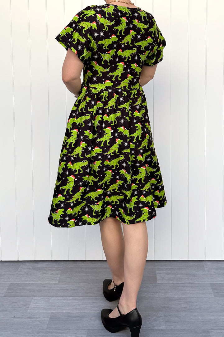 Person wearing a dress with green dinosaurs wearing santa hats on a black background.