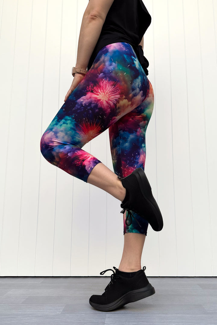 Person wearing colorful firework patterened capri leggings, standing against a white wall.