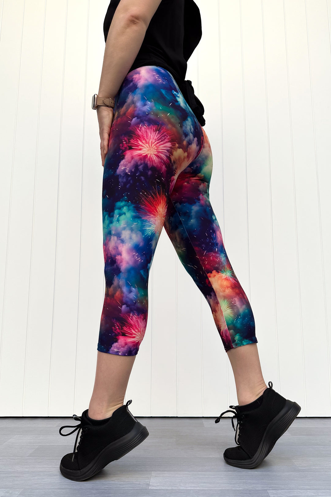 Person wearing colorful firework patterened capri leggings, standing against a white wall.
