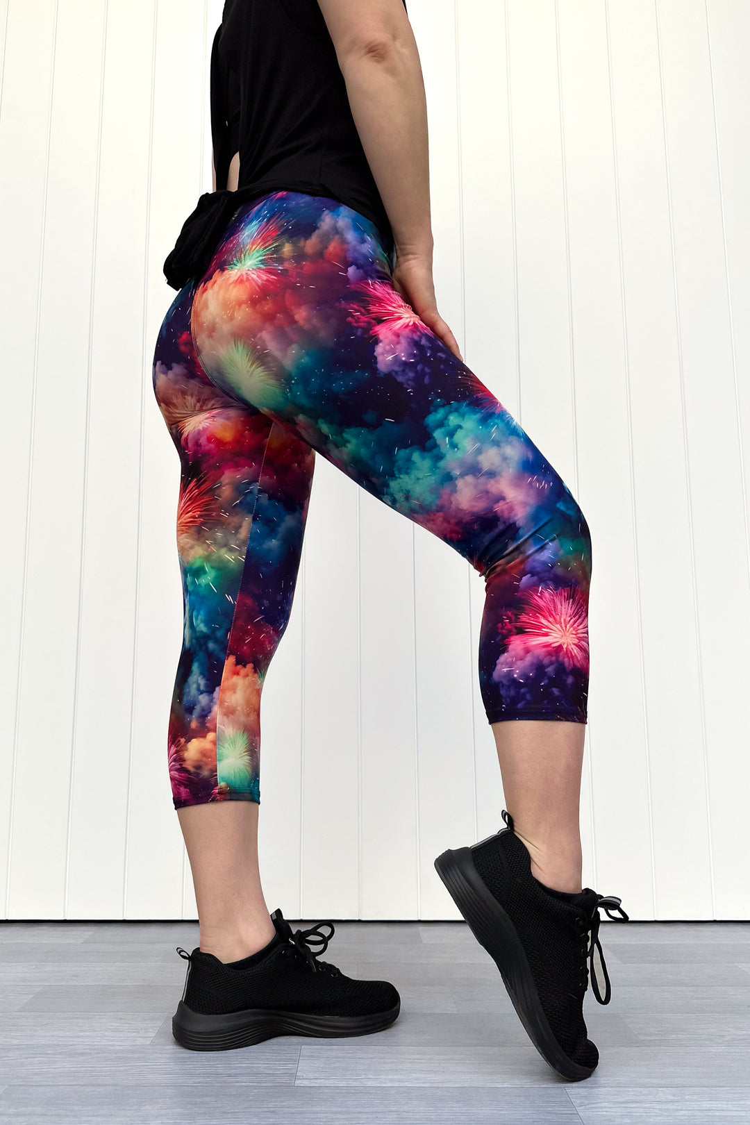 Person wearing colorful firework patterened capri leggings, standing against a white wall.
