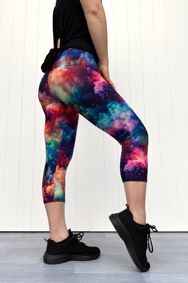 Person wearing colorful firework patterened capri leggings, standing against a white wall.