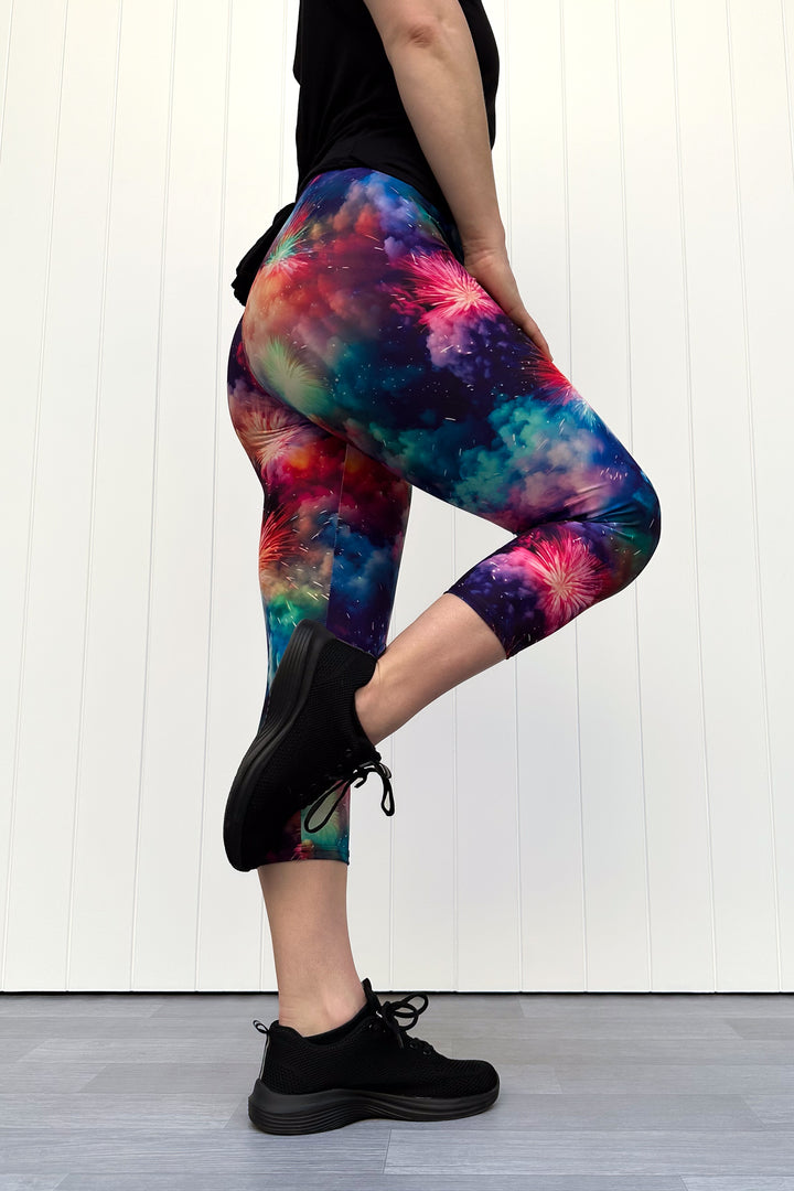 Person wearing colorful firework patterened capri leggings, standing against a white wall.