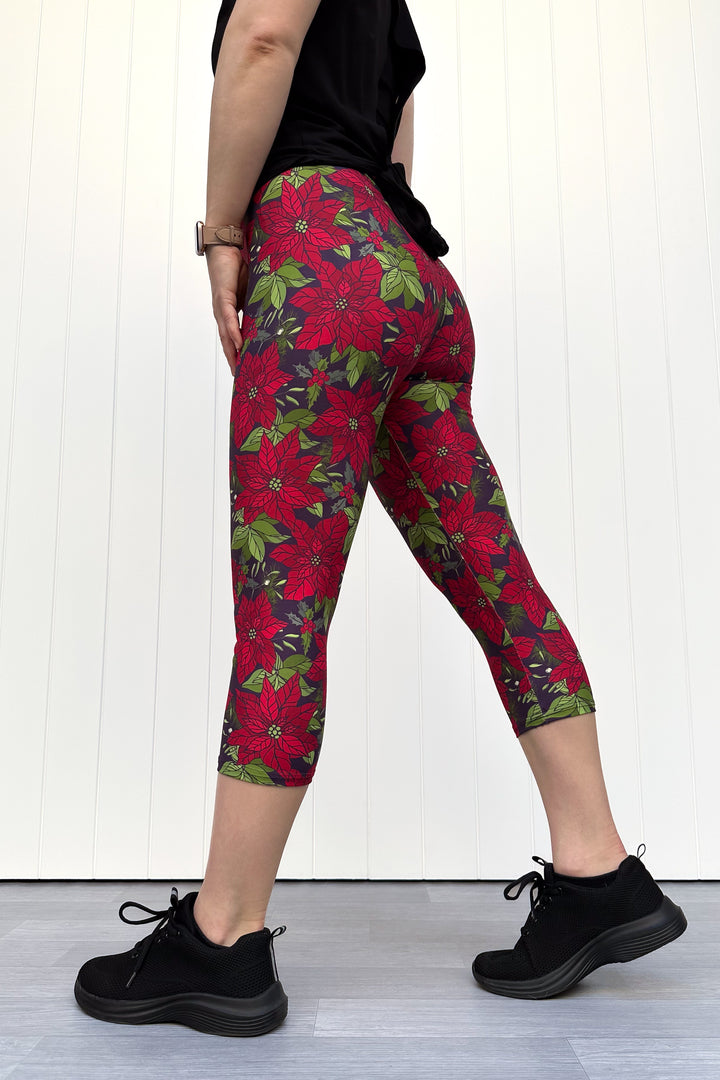 Person wearing red floral Christmas capri leggings, standing against a white wall.