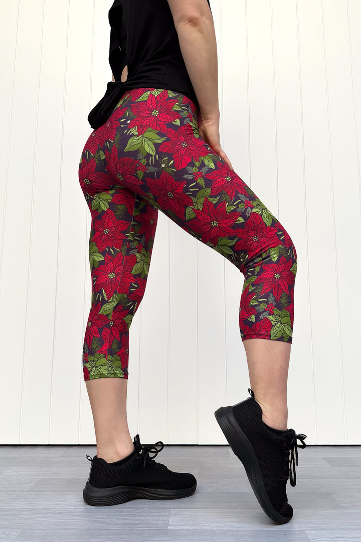 Person wearing red floral Christmas capri leggings, standing against a white wall.