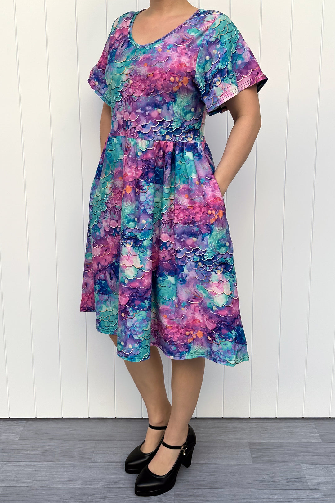 Person wearing a colourful mermaid siren pattern dress against a white wooden panel background