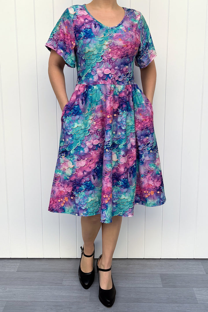 Person wearing a colourful mermaid siren pattern dress against a white wooden panel background